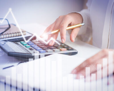 Accountant calculating profit with financial analysis graphs. Notebook, glasses and calculator lying on desk. Accountancy concept. Cropped view.